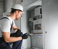 Een man in een blauwe bouwpak en een witte helm legt elektriciteit aan in een appartement.