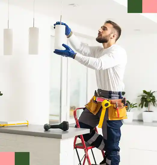 Een man in een bouwpakket hangt een hanglamp op in een pas gerenoveerde keuken.